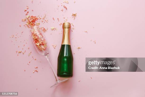 green and golden glass bottle of champagne, glass and golden confetti over pink background. festive new year greeting card. - champagne cork stock pictures, royalty-free photos & images