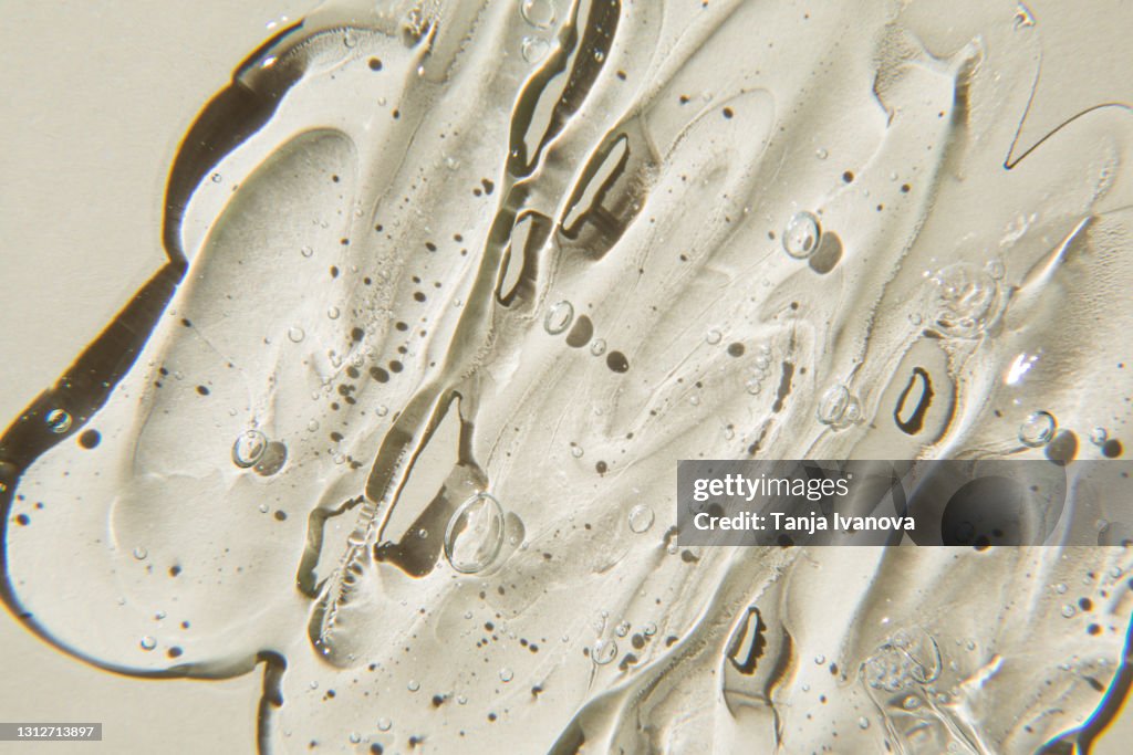 Transparent gel cream cosmetic with bubbles on beige background. Liquid hyaluronic acid gel. Flat lay, top view.