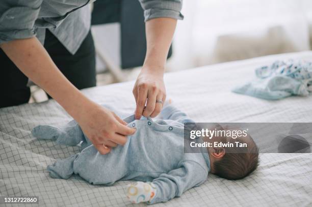 padre chino asiático se pone abotonamiento para su bebé en la cama - vestirse fotografías e imágenes de stock