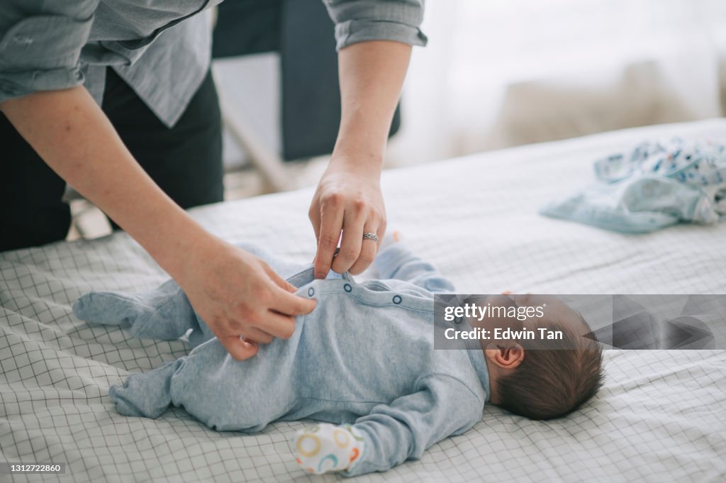 Asian chinese young father putting on buttoning for his baby boy on bed