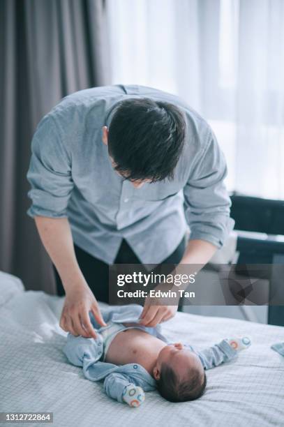 asiatische chinesische junge vater setzen auf knopfdruck für seinen kleinen jungen auf dem bett - babybekleidung stock-fotos und bilder