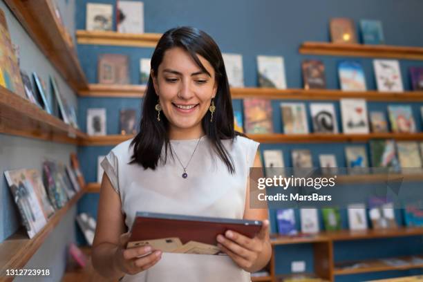 smiling young woman buying books in pretty bookry - children's literature stock pictures, royalty-free photos & images