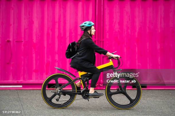 young woman riding electric bike with pink background. - e bike stock pictures, royalty-free photos & images