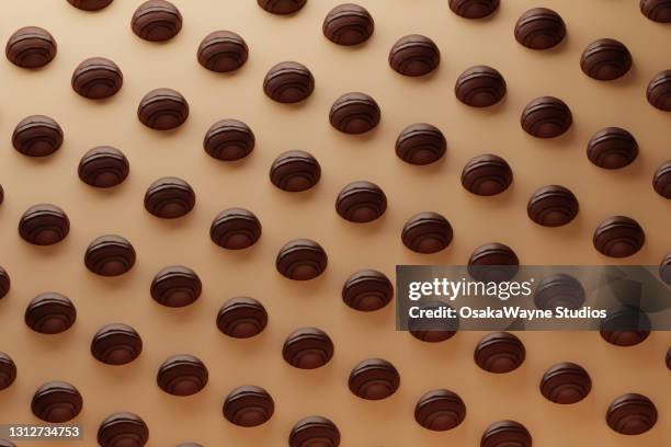 regular grid of chocolate pralines laying on beige board. - praline stock pictures, royalty-free photos & images