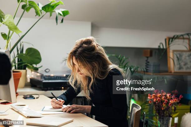 junge kaukasierin, die von zu hause aus arbeitet- in ihrem bürobereich sitzt und notizen schreibt (horizontal) - message stock-fotos und bilder