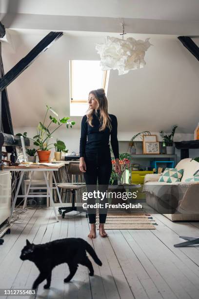 young beautiful caucasian woman standing in the middle of a  bright living room - domestic cat standing stock pictures, royalty-free photos & images