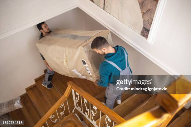 professional movers moving up on staircase and carrying large box with furniture on first floor of house - removal men imagens e fotografias de stock