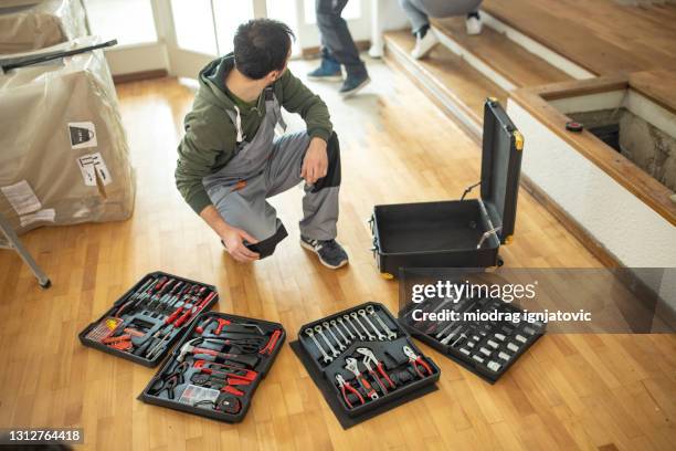 repairman kneeling in front of toolbox and choosing hand tool for work - eastern european man in front of house stock pictures, royalty-free photos & images