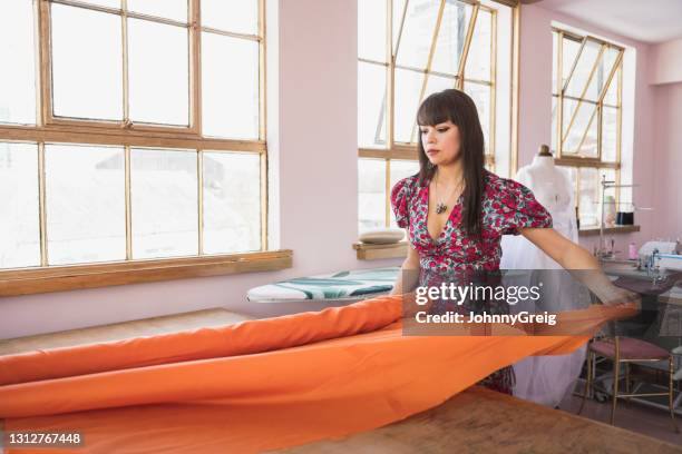 mixed race tailor examining roll of orange fabric in atelier - textile stock pictures, royalty-free photos & images