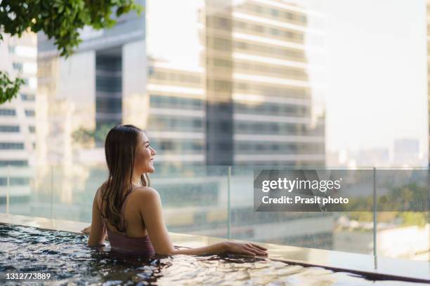 asian woman in swimsuit is swimming in a pool with the city in the background during a long summer vacation. - travel boundless stock-fotos und bilder