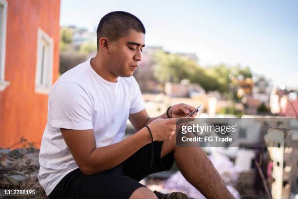 young man texting on smartphone on the street - mexico slums stock pictures, royalty-free photos & images