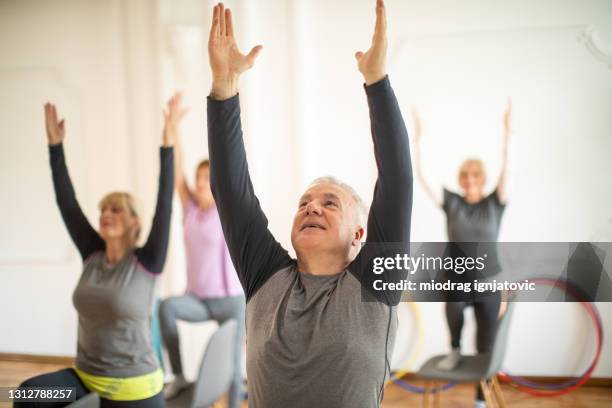 idoso em aula de yoga ao lado de mulheres idosas em estúdio de yoga - cadeira - fotografias e filmes do acervo