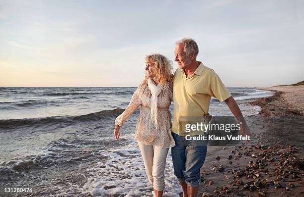 mature couple paddling in sea looking at sunset - senior couple stock pictures, royalty-free photos & images