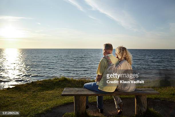 mature couple on bench watching sunset over ocean - young at heart bildbanksfoton och bilder