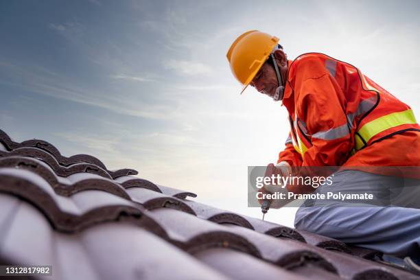 construction worker install new roof, electric drill used on new roofs with tiled roof - dakdekker stockfoto's en -beelden