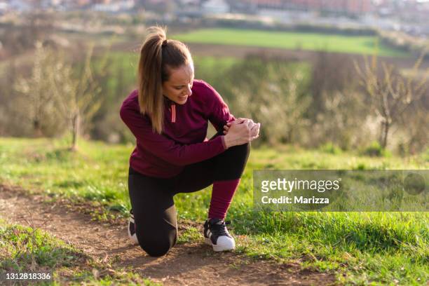 female athlete holding her knee in pain at the park - human knee stock pictures, royalty-free photos & images