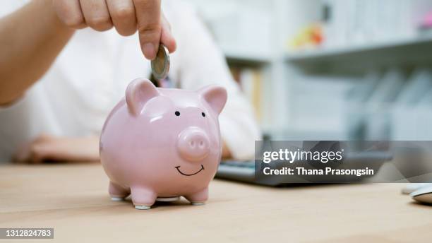 woman hand putting money coin into piggy bank for saving money - piggy bank stock pictures, royalty-free photos & images
