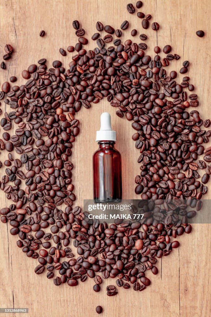 Coffee essential oil in a glass dropper bottle and coffee beans on wooden background