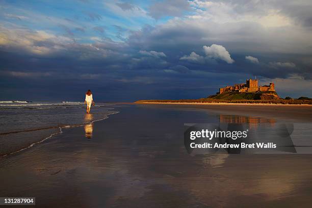 woman walking along a deserted beach - bamburgh castle stock pictures, royalty-free photos & images