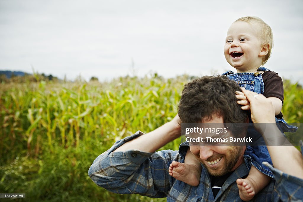 Farmer holding baby boy on shoulders laughing