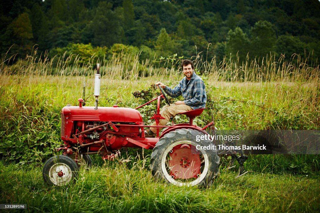 Male farmer driving tractor in field smiling