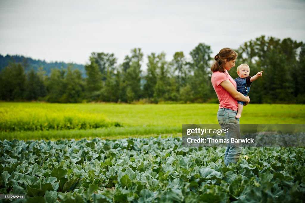 Female farmer holding baby boy in farm field