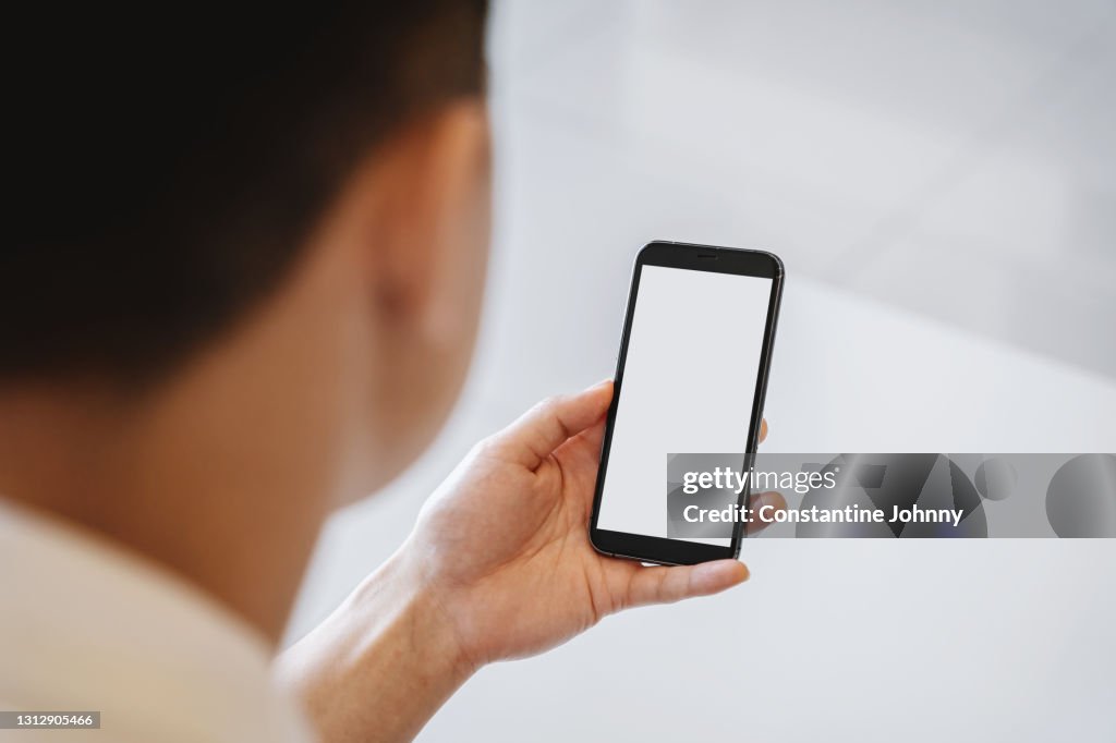 Over The Shoulder View of A Man Using Mobile Phone With Blank White Screen Mock Up