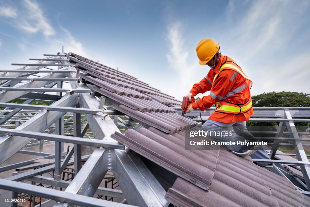 Roofer Construction worker on steel roof frame install new tile roof, Roofing tools, Electric drill used on new tile roof, under construction residential building