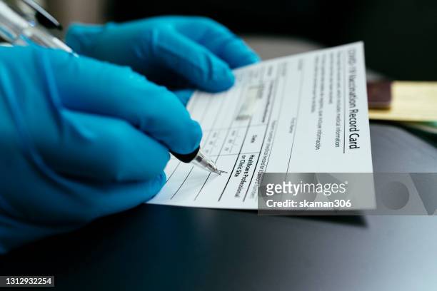 hand of doctor wearing surgical glove and certify vaccination card and passport for first dose vaccine covid-19 (coronavirus) - covid 19 vaccine stock pictures, royalty-free photos & images