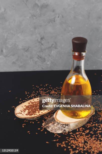 flax seeds in white bowl and a glass bottle of linseed oil on a wooden cutting board on a dark and grey background - black seed oil - fotografias e filmes do acervo