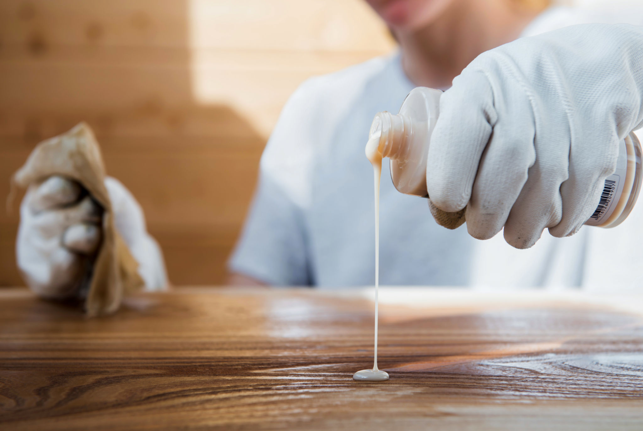 A girl in work gloves pours oil on a wooden tabletop. Coating wood with oil A girl in work gloves pours oil on a wooden tabletop. Coating wood with oil