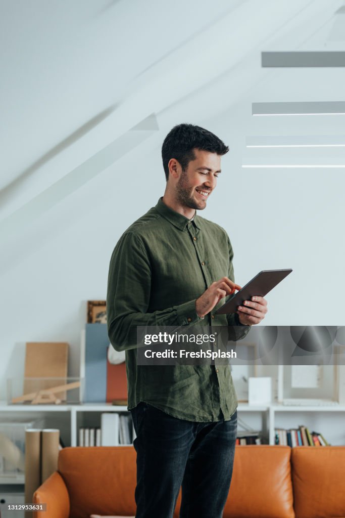 Smiling Man in a Green Shirt Using a Digital Tablet in the Office