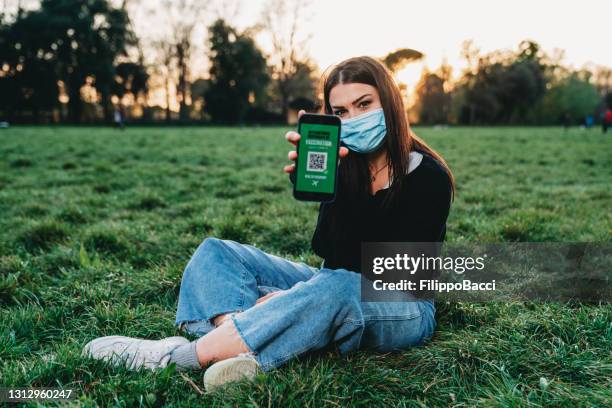 jeune femme affichant un passeport de vaccin covid-19 sur son téléphone intelligent à l’appareil-photo - passeport vaccinal photos et images de collection
