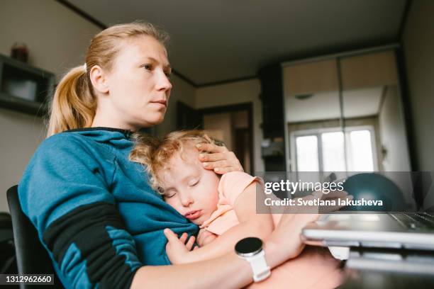 covid-19 working from home. a woman with a sleeping child in her arms sits at a computer and works remotely. - mid adult women imagens e fotografias de stock