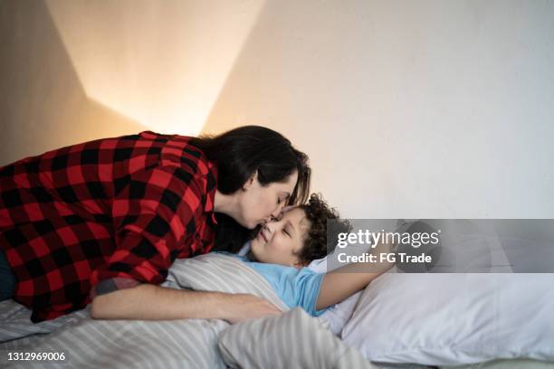 mother putting son to sleep at home - good night kisses stock pictures, royalty-free photos & images