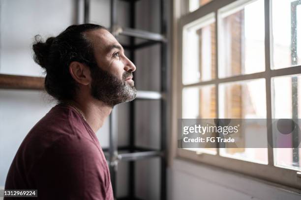uomo che guarda attraverso la finestra di casa - selective focus foto e immagini stock