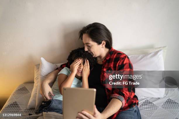 scared girl covering eyes while watching something on digital tablet with mother in bed - enchanted film stock pictures, royalty-free photos & images