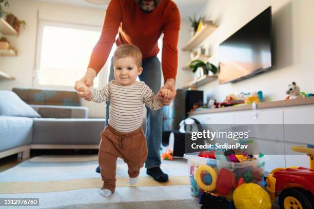 baby boy making first steps with the help of his unrecognizable father - primeiros passos imagens e fotografias de stock