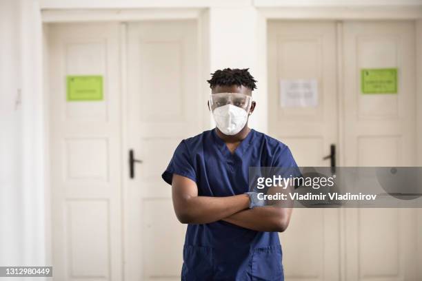 healthcare assistant wearing protective face mask, glasses and gloves stands looking at the camera - black glove stock pictures, royalty-free photos & images