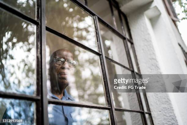 uomo anziano che guarda attraverso la finestra di casa - solitudine foto e immagini stock