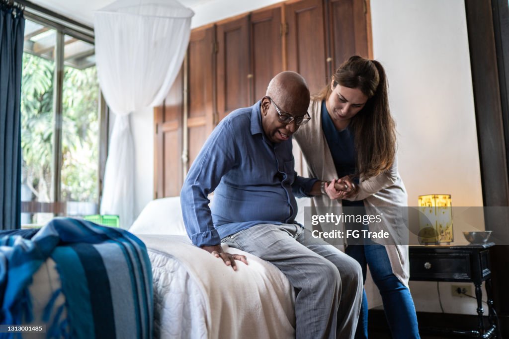 Home caregiver helping a senior man standing up at home