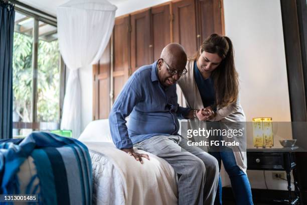 home caregiver helping a senior man standing up at home - care stock pictures, royalty-free photos & images