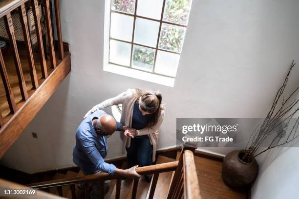 home caregiver helping senior man walking up the stairs at home - staircase house stock pictures, royalty-free photos & images