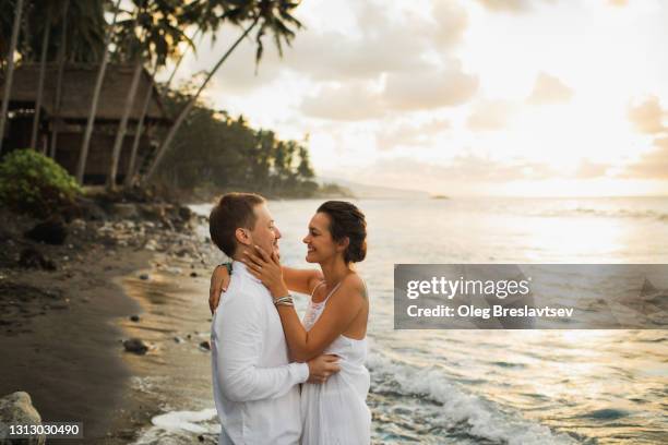 young and happy couple enjoying in love, laughing and hugging. sunset at seaside, shining orange sun light. - flitterwochen stock-fotos und bilder