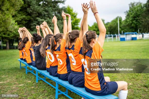 squadra di calcio femminile che alza la mano mentre è seduta su una panchina - divisa sportiva foto e immagini stock