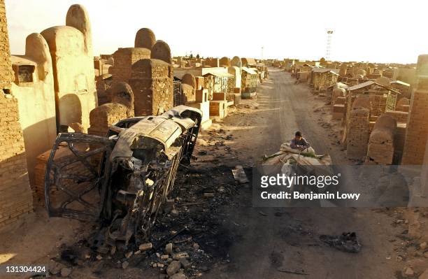 Donkey riding Iraqi boy with a bundle of produce, passes the burnt wreck of an Iraqi militia vehicle destroyed during a battle with American forces...