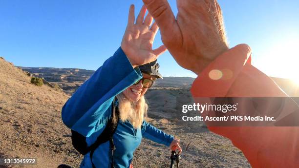 portrait of mature woman mountain biker high-fiving friend - glen haven co stock pictures, royalty-free photos & images