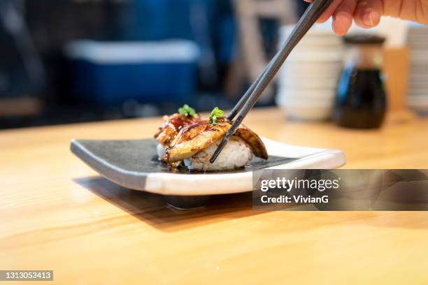 een hand die japanse sushi van foie gras met eetstokjes opneemt - nigiri stockfoto's en -beelden