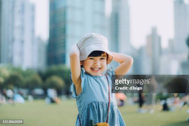 portrait of happy little asian girl having fun playing in urban park, smiling joyfully. enjoying freedom and beauty of nature. with modern cityscape in background - happy toddler stockfoto's en -beelden