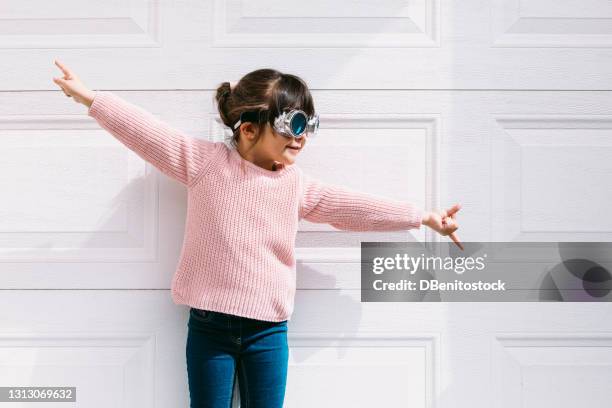small black haired girl smiling wearing pink sweater and victorian glasses, arms outstretched in white garage door - golden goggles stock pictures, royalty-free photos & images